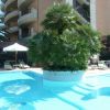 Piscina con palme centrali, ombrelloni bianchi e edificio sullo sfondo.