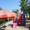 Parco giochi con scivolo colorato e grande ombrellone arancione.