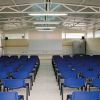 Aula spaziosa con sedie blu rivolte verso uno schermo bianco.