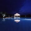 Piscina illuminata di notte con gazebo centrale e cielo scuro.
