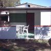 Bungalow con veranda e sedie bianche in plastica, circondato da un muretto in un giardino.