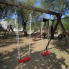 Altalene rosse e scivolo in un parco giochi all'aperto con alberi.