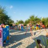Un'area giochi sulla spiaggia con strutture colorate e bambini che giocano nella sabbia.