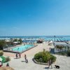 Area balneare con piscina, spazi verdi e lettini sotto ombrelloni azzurri.