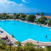 Piscina azzurra con lettini e ombrelloni in un resort, cielo sereno sullo sfondo.
