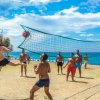 Persone giocano a beach volley su un prato vicino al mare. Cielo azzurro.