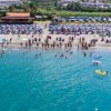 Spiaggia affollata con ombrelloni blu, persone che nuotano e un mare limpido.
