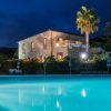 Edificio in pietra illuminato di notte, davanti a una piscina e palme sullo sfondo.