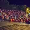 Grande folla riunita su gradinate all'aperto di notte, circondata da palme.