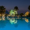 Piscina illuminata di notte circondata da palme e ombrelloni.