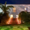 Edificio in pietra con scale illuminate e vegetazione.