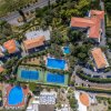 Vista aerea di un complesso con piscine e campi da tennis circondati da vegetazione.