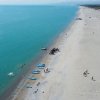 Lunga spiaggia con canoe e persone sul bagnasciuga.