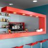 Interno di un bar moderno con bancone rosso, sgabelli e una macchina da caffè.