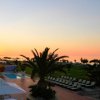 Tramonto su un resort con piscina, palme e sedie a sdraio.