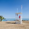 Spiaggia sabbiosa con torretta di salvataggio bianca, mare calmo e cielo azzurro.