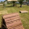 Area all'aperto con attrezzature in legno per allenamento e palme sul prato.