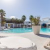 Piscina con palme e archi lontani, area relax con cuscini sulla sinistra.