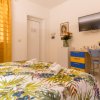 Interno di camera con letto matrimoniale, TV, scrivania con sedia blu e tenda arancione.