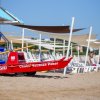 Una barca di salvataggio rossa sulla spiaggia con sedie a sdraio e ombrelloni.