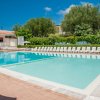 Piscina con lettini bianchi e ombrelloni, immersa nel verde e con cielo blu.
