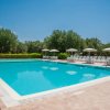Piscina con ombrelloni e lettini bianchi, circondata da alberi verdi e cielo sereno.