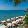 Spiaggia con ombrelloni bianchi e lettini, bagnanti in mare e una vista su una piccola isola.