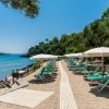 Spiaggia sabbiosa con lettini e ombrelloni bianchi vista mare e colline.
