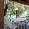 Tavolo bianco con sedie sotto un portico circondato da alberi.