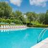 Piscina all'aperto con lettini bianchi, circondata da alberi e cielo blu.