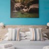 Letto matrimoniale con cuscini a righe, parete blu, foto di cascata e applique tonde.