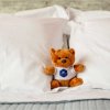 Orsetto di peluche su cuscini bianchi, indossa una maglietta con logo blu.