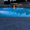 Piscina illuminata di sera con ombrelloni e lettini intorno.