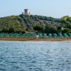 Spiaggia con file ordinate di ombrelloni verdi e una torre su una collina sullo sfondo.