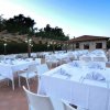 Tavoli all'aperto apparecchiati con tovaglie bianche e sedie su una terrazza, sotto una pergola.
