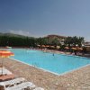 Piscina all'aperto con lettini e ombrelloni colorati. Persone in acqua e cielo sereno.