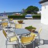 Tavoli e sedie gialle su un terrazzo, con piscina e alberi sullo sfondo.