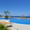 Piscina con lettini, ombrelloni a strisce e vista mare.