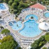 Complesso acquatico con piscine, ombrelloni e scivoli, circondato da alberi e un'area giochi.