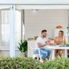 Coppia beve bevande a un tavolo all'aperto con piatti di frutta, davanti a una casa vacanze moderna.