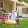 Bambine con gonfiabile unicorno su prato, famiglia a tavola sullo sfondo.